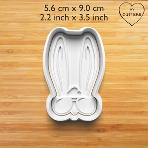 May include: White plastic cookie cutter shaped like a bunny wearing sunglasses. The cutter measures 5.6 cm by 9.0 cm.