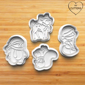 May include: Four white plastic cookie cutters shaped like a deer, a squirrel, a penguin, and a snowman. The cutters are on a wooden surface.