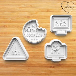 May include: Four white cookie cutters with tech-themed designs. One is a bitten cookie with "I'm deleting cookies" text. Others include a computer screen with "404 Not Found", a warning sign with "404", and a screen with a sad face and "404".