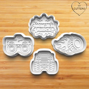 May include: Four white plastic cookie cutters. The shapes include a monster truck, a flaming tyre, and a text bubble with "MONSTER TRUCK". The cutters are displayed on a wooden surface.