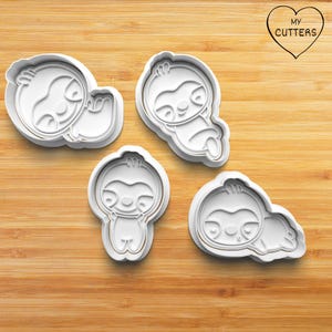 Può includere: Quattro stampini per biscotti in plastica bianca a forma di bradipi in varie pose. Ogni stampino presenta un contorno in rilievo per impressioni dettagliate. Un logo a forma di cuore contiene il testo MY CUTTERS in lettere nere.