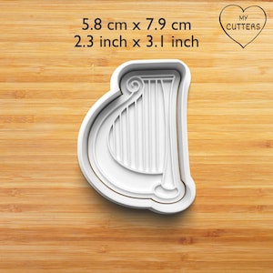 Könnte beinhalten: Ein weißer harfenförmiger Ausstecher mit Rahmen und Innendetails. Der Text 5.8 cm x 7.9 cm und 2.3 inch x 3.1 inch ist über dem Objekt sichtbar, zusammen mit einem Herzlogo mit dem Text MY CUTTERS in der oberen rechten Ecke.
