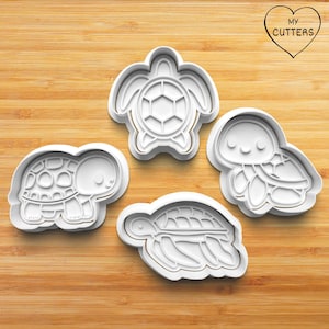 May include: Four white plastic cookie cutters shaped like sea turtles. The cutters are on a wooden surface. The cutters are for making cookies or other baked goods.