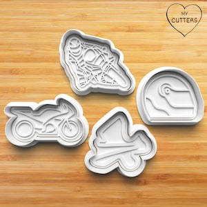 May include: Four white plastic cookie cutters shaped as a motorcycle, a motorcycle racer, a racing helmet, and a racing track. The cutters are on a wooden surface. The text "MY CUTTERS" is inside a heart shape.