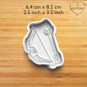 Könnte beinhalten: Weißer Plastik-Ausstecher in Form eines Pfeils und Bogens mit floralen Details. Der Ausstecher misst 6,4 cm x 8,2 cm.