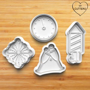 May include: Four white plastic cookie cutters shaped like a clock face, a snowflake, a champagne toast, and a firecracker. The cutters are on a wooden surface. My Cutters is printed on a heart-shaped sticker.