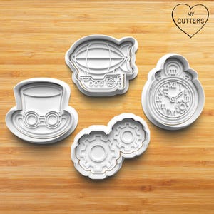 May include: A selection of white plastic cookie cutters in steampunk designs. The cutters feature a top hat with goggles, a blimp, a pocket watch, and two interlocking gears. The cutters are on a wooden surface.