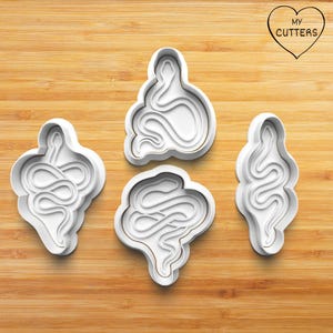 Könnte beinhalten: Vier weiße Ausstechformen aus Kunststoff in Form von gewundenen Schlangen. Jede Form zeigt eine eigene Schlangensilhouette mit inneren Rillen für Details. Der Text MY CUTTERS ist in Schwarz in einem Herzumriss in der oberen rechten Ecke gedruckt.