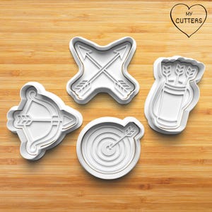 Könnte beinhalten: Vier weiße Ausstecher in Bogenschützen-Formen: ein Bogen mit Pfeil, gekreuzte Pfeile, ein Köcher mit Pfeilen und eine Zielscheibe mit Pfeil. Die Ausstecher liegen auf einer Holzoberfläche, mit dem Text "MY CUTTERS" in einem Herz.