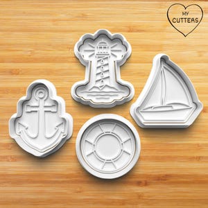 May include: Four white plastic cookie cutters in nautical shapes: an anchor, a lighthouse, a life preserver, and a sailboat. The lighthouse is atop a cloud-like base. The sailboat has a triangular sail. The cutters are on a wooden surface.