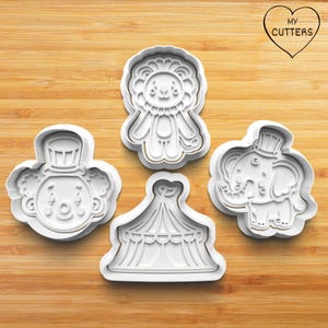 Könnte beinhalten: Vier weiße Ausstecher aus Kunststoff in Form von Zirkusfiguren. Die Formen umfassen einen Löwen, einen Clown, einen Elefanten und ein Zirkuszelt. Die Ausstecher befinden sich auf einer Holzoberfläche. Der Text "MY CUTTERS" ist herzförmig.