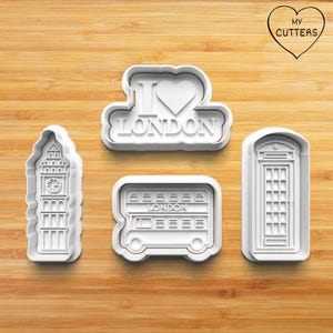 Op de afbeelding: Vier witte plastic koekjessnijders in de vorm van Londense bezienswaardigheden. Inclusief Big Ben, een dubbeldekkerbus, een telefooncel en een "I Love London"-ontwerp. De uitstekers liggen op een houten oppervlak.