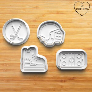 Könnte beinhalten: Ein Set aus vier weißen Kunststoff-Ausstechformen zum Thema Eishockey: eine runde Form mit gekreuzten Hockeyschlägern und Puck, ein Helm, ein Schlittschuh und eine rechteckige Eisfläche. Das Logo MY CUTTERS befindet sich oben rechts.