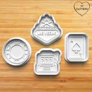 May include: Set of four white plastic cookie cutters shaped like a casino chip, a slot machine, a playing card, and a welcome to Las Vegas sign.