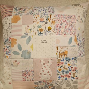 May include: A square patchwork cushion featuring a variety of fabric squares with floral, animal, and striped patterns in soft pastel colours. One square displays the text hello world, and a central square features a white rabbit appliqu&eacute;.