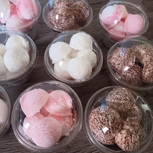 May include: An assortment of desserts in clear plastic containers. Some contain pink and white scoops, others white scoops, and some have brown, speckled spheres. The containers have clear, dome-shaped lids.