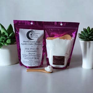 May include: Two purple pouches of bath and foot soak products, with a wooden scoop and two small potted succulents. The pouches are labeled "Whispers From Serenity" and contain Apple Cider Vinegar, Tea Tree Oil, and Lavender.