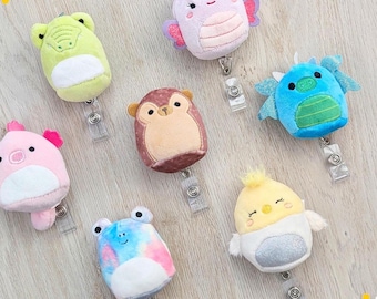 May include: A collection of plush badge reels in various animal shapes, including a frog, butterfly, monkey, dragon, pig, and chick. Each reel is a different color and has a retractable cord and a clear plastic clip.