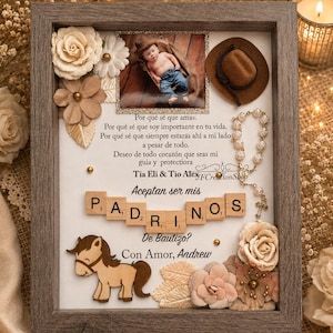 Puede incluir: Un marco tipo caja con una foto de un bebé, un sombrero marrón en miniatura, un rosario blanco y fichas de madera con la palabra PADRINOS. Incluye flores de tela, una figura de caballo de madera y texto en español solicitando el bautizo.