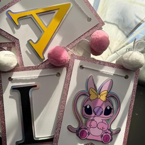 May include: A banner with white pennants, each outlined with pink glitter. The banner spells out "I LOVE" with yellow and black letters. A pink cartoon character with a yellow bow is featured on one pennant, and pink and white pom-poms are attached.