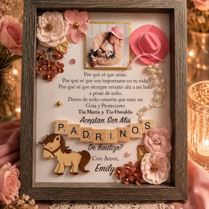 May include: A shadow box frame containing a photograph of a baby, a miniature pink cowboy hat, a string of pearls, and wooden letter tiles spelling "PADRINOS". The text reads "Por qué sé que amas... Aceptan Ser Mis Padrinos De Bautizo? Con Amor, Emily".