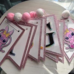 May include: A pink and white banner with glitter trim and pom-poms. Each pennant features a cartoon character with a yellow bow. The banner spells out "1st" with a cartoon character on each side.