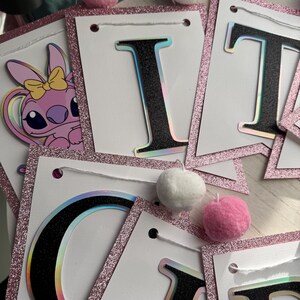 May include: A banner with white pennants, outlined with pink glitter, and black letters with a holographic effect. The banner is decorated with pink and white pom-poms. A pink cartoon character with a yellow bow is visible.