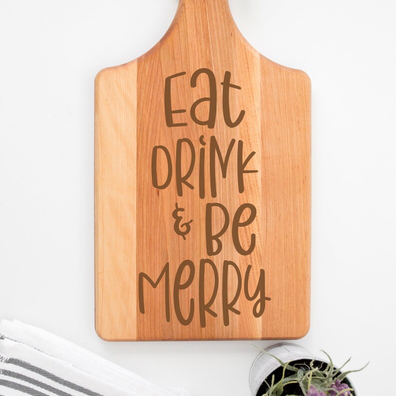 May include: A wooden cutting board with the text "Eat Drink & Be Merry" engraved in brown lettering.