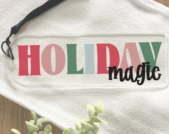 Könnte beinhalten: Ein klarer Acryl-Lesezeichen mit den Worten "HOLIDAY magic" in bunten Blockbuchstaben. Die Buchstaben sind rot, rosa, grün und blau. Eine schwarze Quaste hängt von der Oberseite des Lesezeichens.