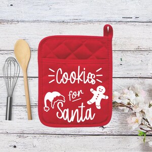 May include: Red quilted oven mitt with the text "Cookies for Santa" in white. The mitt features a Santa hat and gingerbread man graphic. A wooden spoon and whisk are to the left.