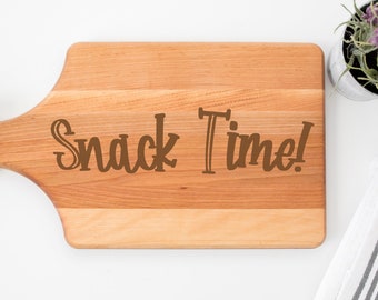 May include: A wooden cutting board with a handle, featuring the text "Snack Time!" engraved in brown lettering.
