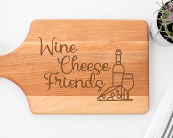 May include: A wooden cutting board with a handle, engraved with the text "Wine Cheese Friends" and a graphic of a wine bottle, a glass of wine, and a wedge of cheese.