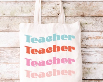 Può includere: Una borsa tote in tela color crema con due manici, caratterizzata dalla parola "Teacher" stampata quattro volte in un design ondulato e sovrapposto. Il testo appare in quattro colori distinti: azzurro, arancione corallo, rosa acceso e rosa chiaro.