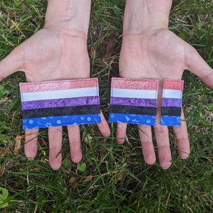 May include: Two fabric patches featuring the genderqueer pride flag design. The larger patch is on the left and the smaller patch is on the right. Both patches have a pink, white, purple, black, and blue colour scheme.