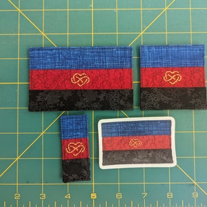 Puede incluir: Cuatro tama&ntilde;os diferentes de una bandera del orgullo poliamoroso. La bandera es azul, roja y negra con un s&iacute;mbolo de coraz&oacute;n entrelazado dorado en el centro.