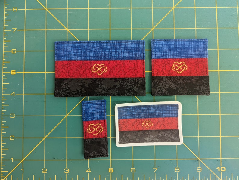 Puede incluir: Cuatro tama&ntilde;os diferentes de una bandera del orgullo poliamoroso. La bandera es azul, roja y negra con un s&iacute;mbolo de coraz&oacute;n entrelazado dorado en el centro.