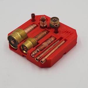 以下が含まれることがあります： さまざまな金属溶接部品を収納する赤いプラスチック製のオーガナイザー。部品には、真鍮色のノズル、銅色のチップ、その他の部品が含まれます。トレイは長方形で、いくつかのコンパートメントがあります。