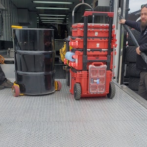 Puede incluir: Un contenedor de almacenamiento apilable rojo con ruedas, sentado en un piso de metal. El contenedor est&aacute; lleno de herramientas y equipos.