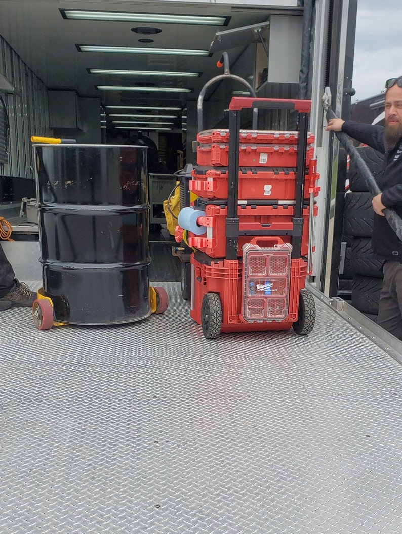 Puede incluir: Un contenedor de almacenamiento apilable rojo con ruedas, sentado en un piso de metal. El contenedor est&aacute; lleno de herramientas y equipos.