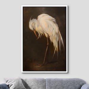 May include: A framed artwork depicting a white egret with its head bowed, highlighting the intricate details of its feathers. The bird is positioned on one leg against a dark brown backdrop, creating a contrast. The artwork is presented in a white frame.
