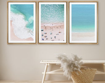Può includere: Tre stampe incorniciate di una scena di spiaggia con acqua turchese, sabbia bianca e persone sulla spiaggia. Le stampe sono in cornici dorate e sono appese a una parete beige chiaro.