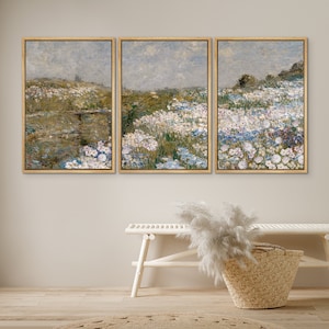May include: Three framed landscape paintings with a muted color palette. The paintings depict a field of white flowers with a blurred background of green foliage and a blue sky.