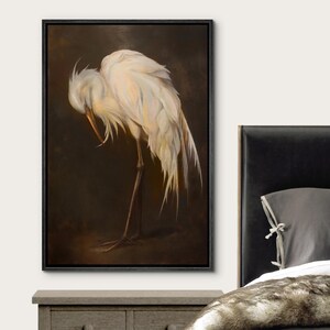 May include: A framed canvas print of a white egret, head bowed, against a dark brown backdrop. The bird's feathers are detailed with soft shading. The artwork is presented in a black frame, ideal for interior decoration and home decor.