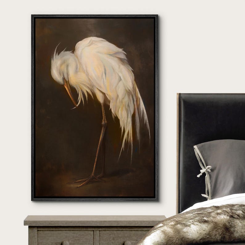 May include: A framed canvas print of a white egret, head bowed, against a dark brown backdrop. The bird's feathers are detailed with soft shading. The artwork is presented in a black frame, ideal for interior decoration and home decor.