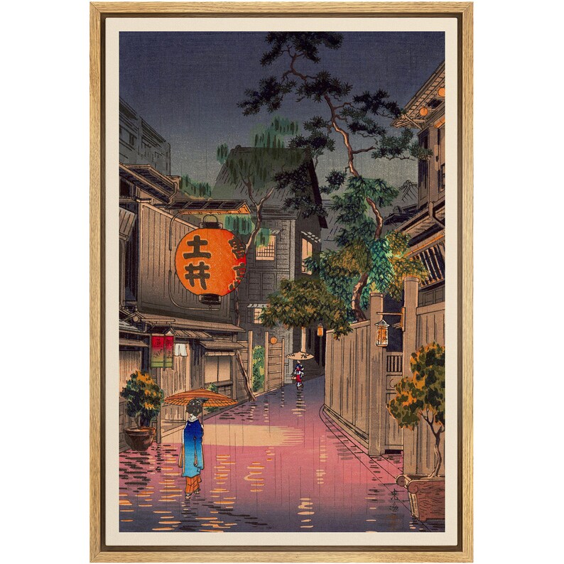 May include: A woodblock print depicting a rainy night scene in a Japanese city. The print shows a narrow street lined with traditional wooden buildings, with a woman walking under an umbrella in the foreground. The street is wet from the rain, and the buildings are illuminated by lanterns. The print is framed in a wooden frame.