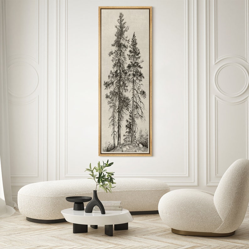 May include: A framed vertical art print featuring a detailed black and white illustration of several tall pine trees. The artwork is set against a neutral background and framed in a gold-toned wood. The print is displayed in a modern, minimalist living room setting.