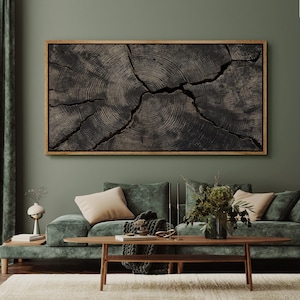 May include: A framed, dark wood art piece depicting the cross-section of a tree trunk, showcasing concentric rings and cracks. The artwork is mounted on a green wall above a green velvet sofa with beige pillows and a wooden coffee table.