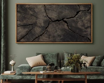 May include: A framed, dark wood art piece depicting the cross-section of a tree trunk, showcasing concentric rings and cracks. The artwork is mounted on a green wall above a green velvet sofa with beige pillows and a wooden coffee table.