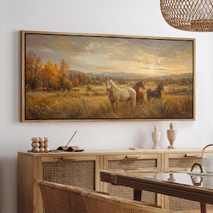 May include: A rectangular landscape painting in a dark frame depicting three horses standing in a golden field during sunset. The scene features autumn trees, distant mountains, and a warm, glowing sky with soft clouds above the grassy meadow.