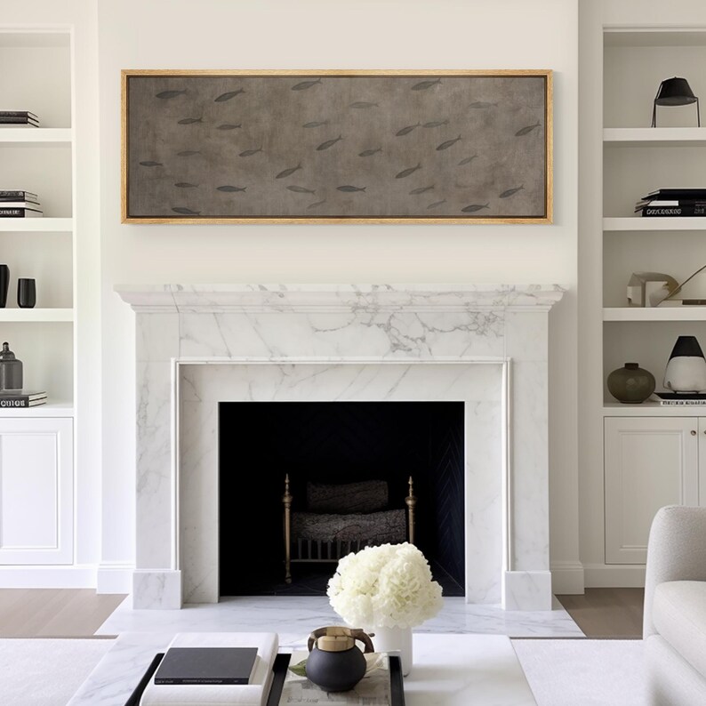 Puede incluir: Obra de arte rectangular enmarcada con peces sobre un fondo gris, sobre una chimenea de m&aacute;rmol blanco. La habitaci&oacute;n tiene estanter&iacute;as blancas a ambos lados de la chimenea. El marco es de color madera clara. La decoraci&oacute;n es en tonos neutros.